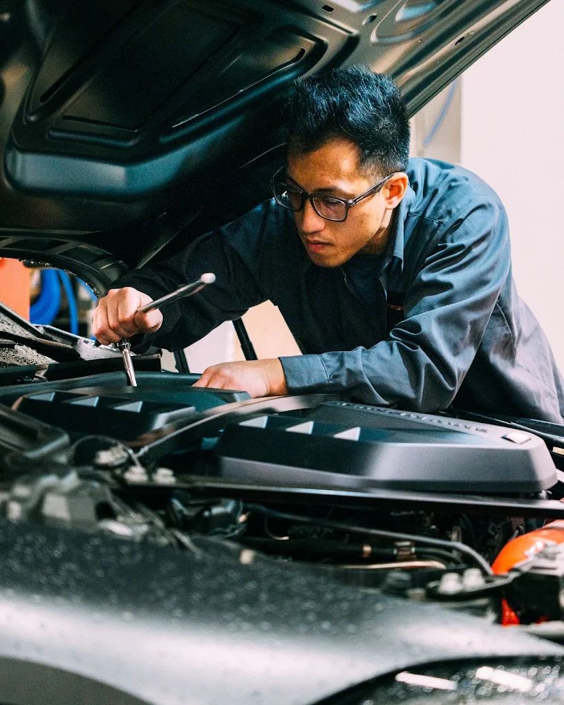Technician with a wrench working under the hood of a car