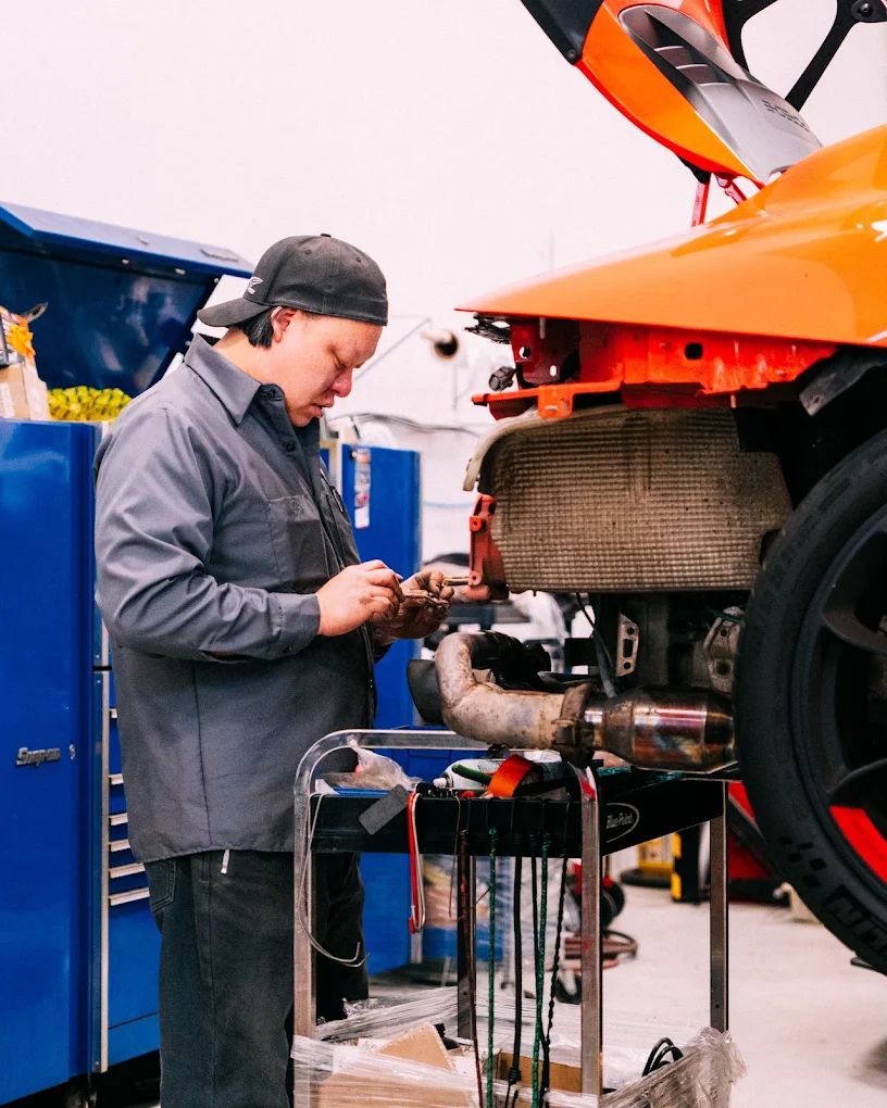 Technician at a tool cart beside an orange race car